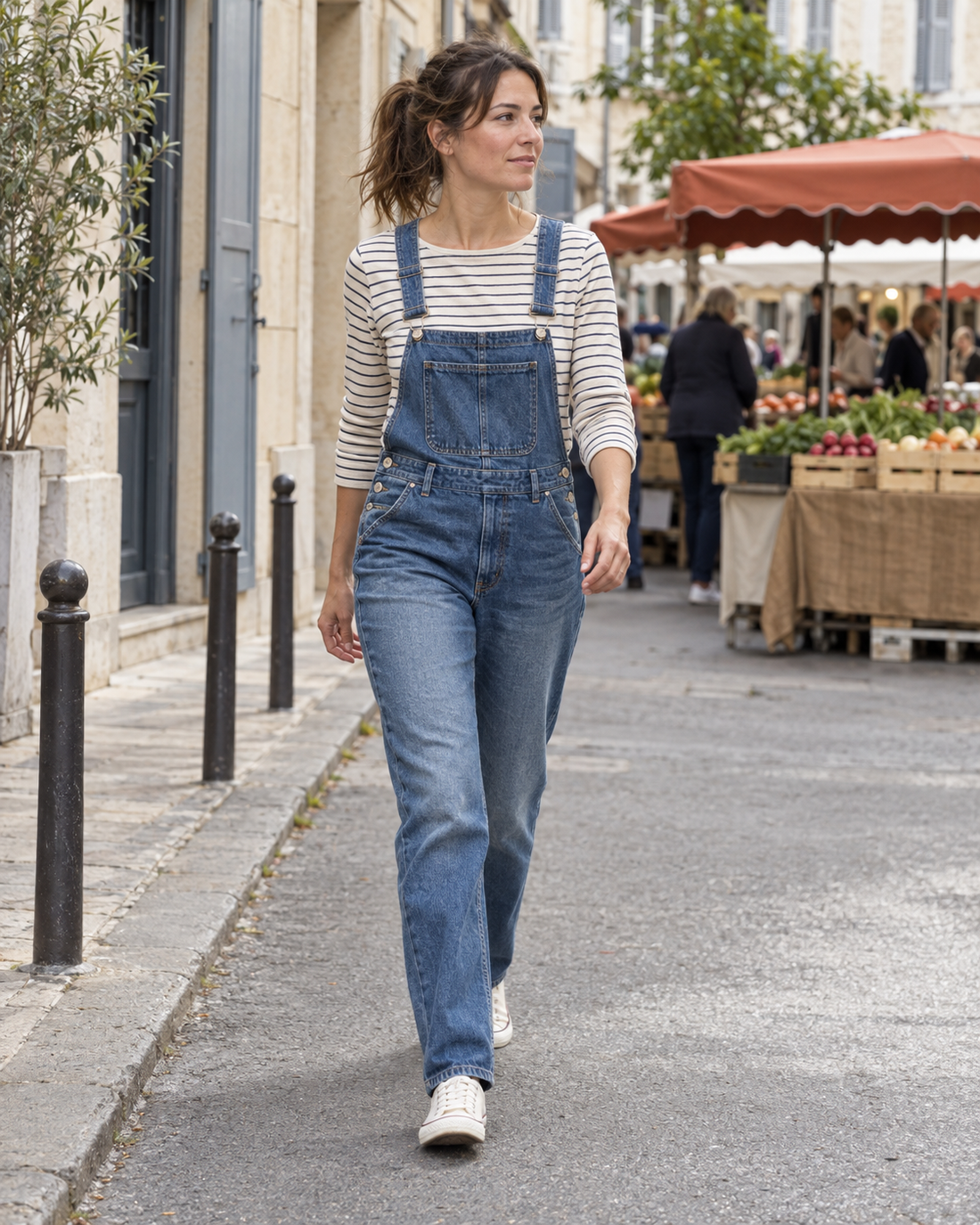 Une femme en salopette denim et marinière marche près d’un marché.