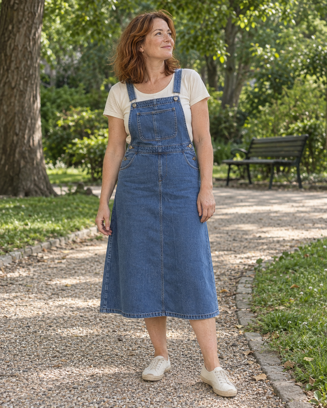 Une femme porte une robe salopette en denim midi dans un jardin.